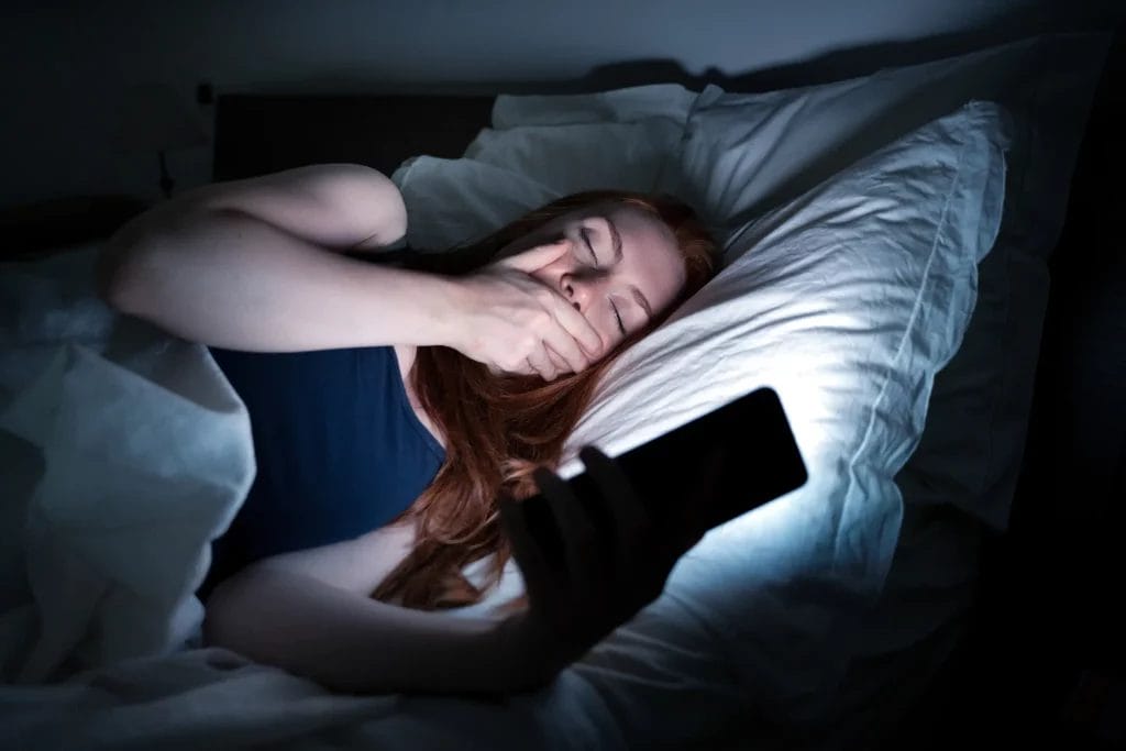 Fatiguée dans son lit devant son smartphone