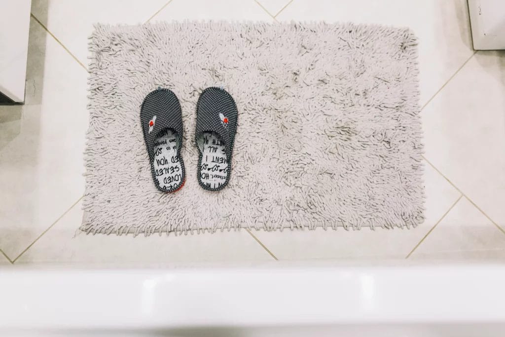 Paire de pantoufles posées sur un tapis de bain gris