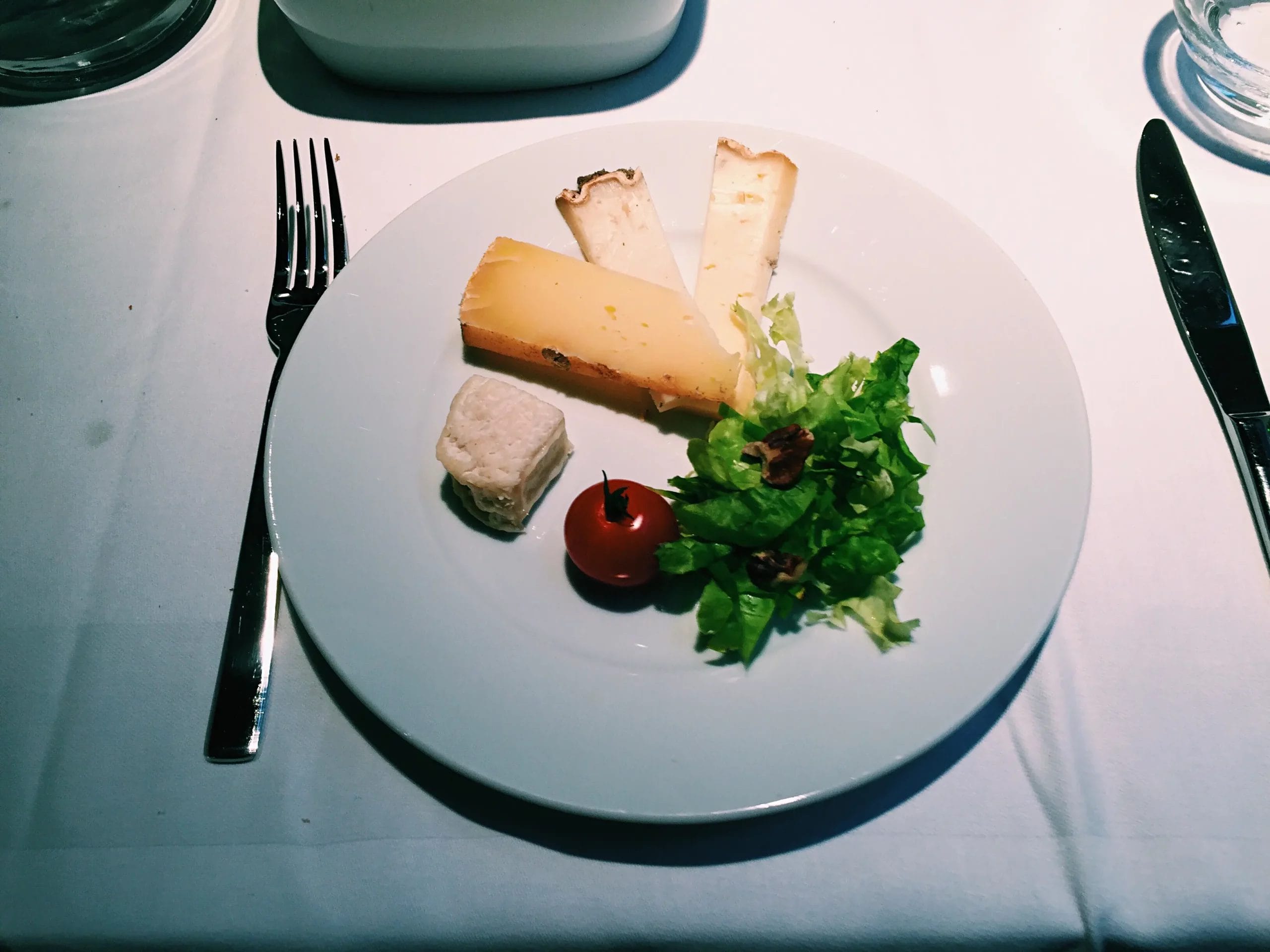 Assiette du soir composée de fromages, salade verte, noix et tomate cerise sur table élégamment dressée.