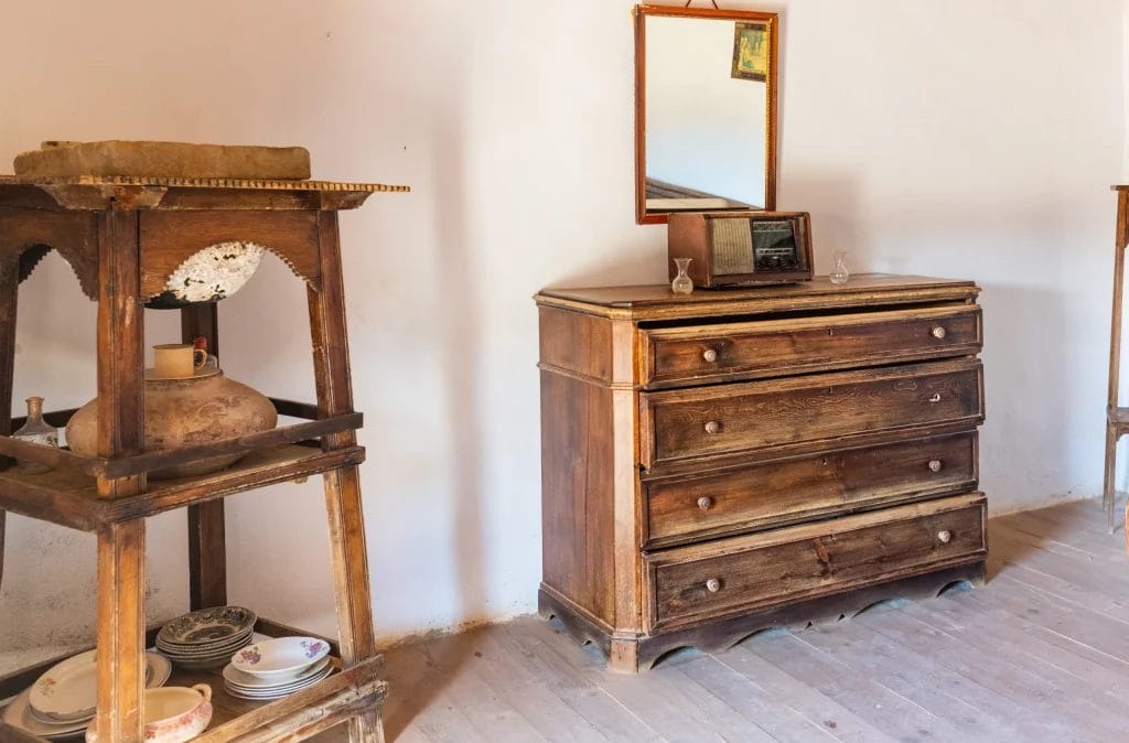 Chaise en bois devant une table rustique avec miroir et vase fleuri.