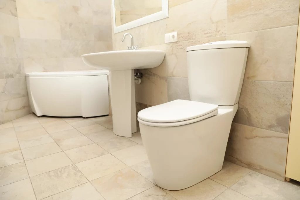 Salle de bain moderne beige avec toilettes, lavabo et baignoire d’angle.